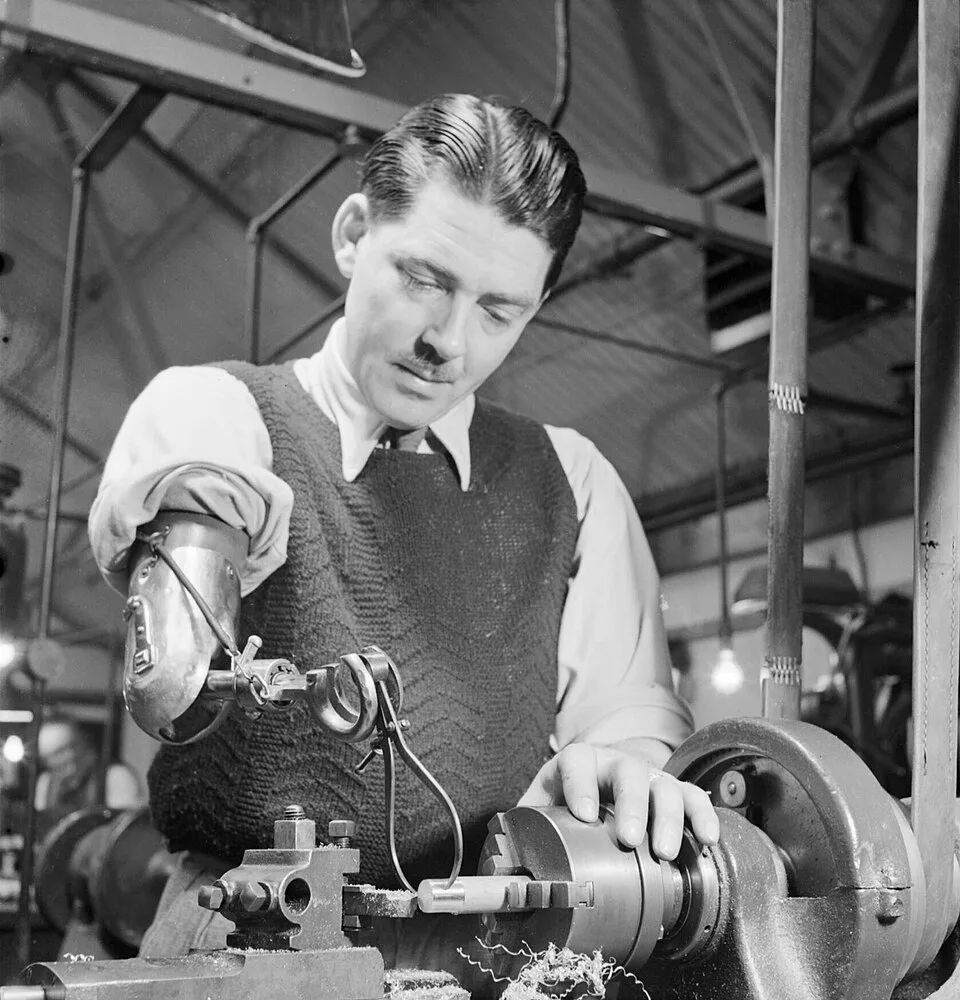 Pracownik fabryki wykorzystujący protezę body-powered. Domena publiczna.